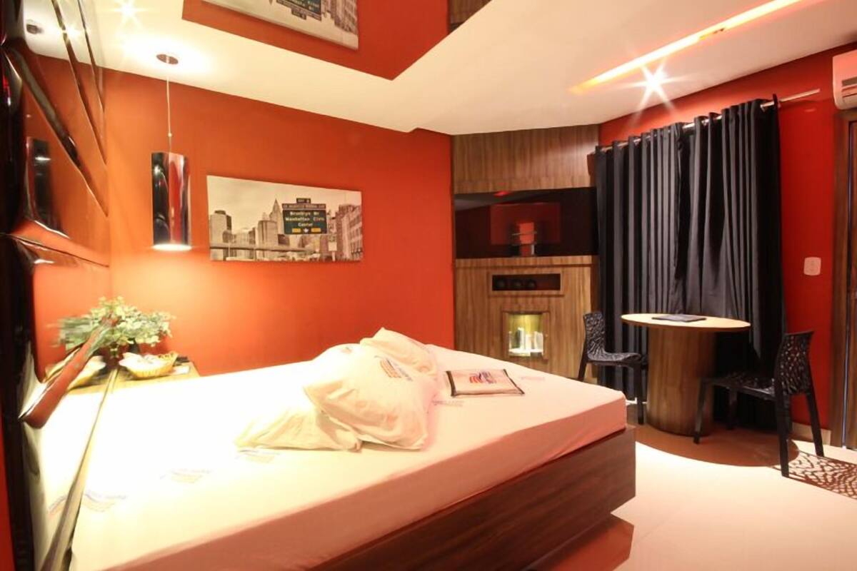 Une chambre d’hôtel avec un lit, une petite table et des chaises, un téléviseur fixé au mur et un tableau représentant un paysage urbain.