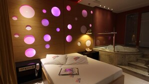Habitación de hotel moderna con una cama grande, una silla de masaje, una bañera de hidromasaje y una pared con diseños de luces circulares.