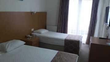 A hotel room with two beds, a bedside table with a phone, a radiator, and a window with curtains.