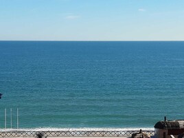 A coastal view with a clear sky, a calm sea, and a metal railing along the shore.