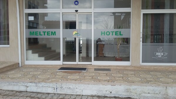 A hotel entrance with glass doors, a sign for 'MELTEM' on the left, and a 'HOTEL' sign on the right.