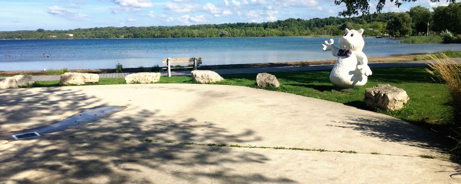 A concrete pathway leading to a grassy area with a bench and a large white sculpture.