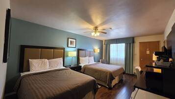 A hotel room with two beds, a ceiling fan, a desk with a coffee maker, and a door with a 'No Smoking' sign.