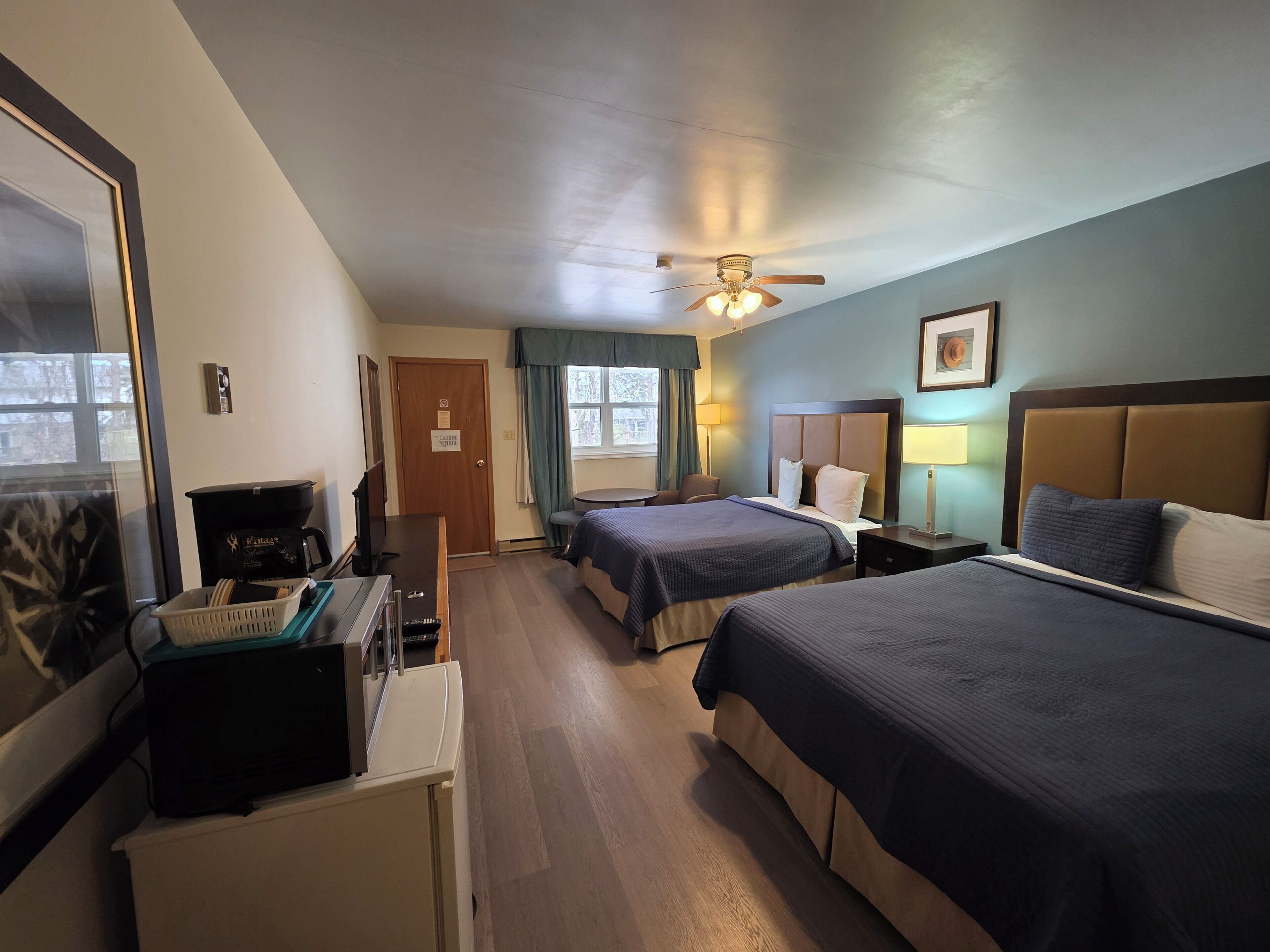 A hotel room with two beds, a desk with a coffee maker, a television, and a window with curtains.