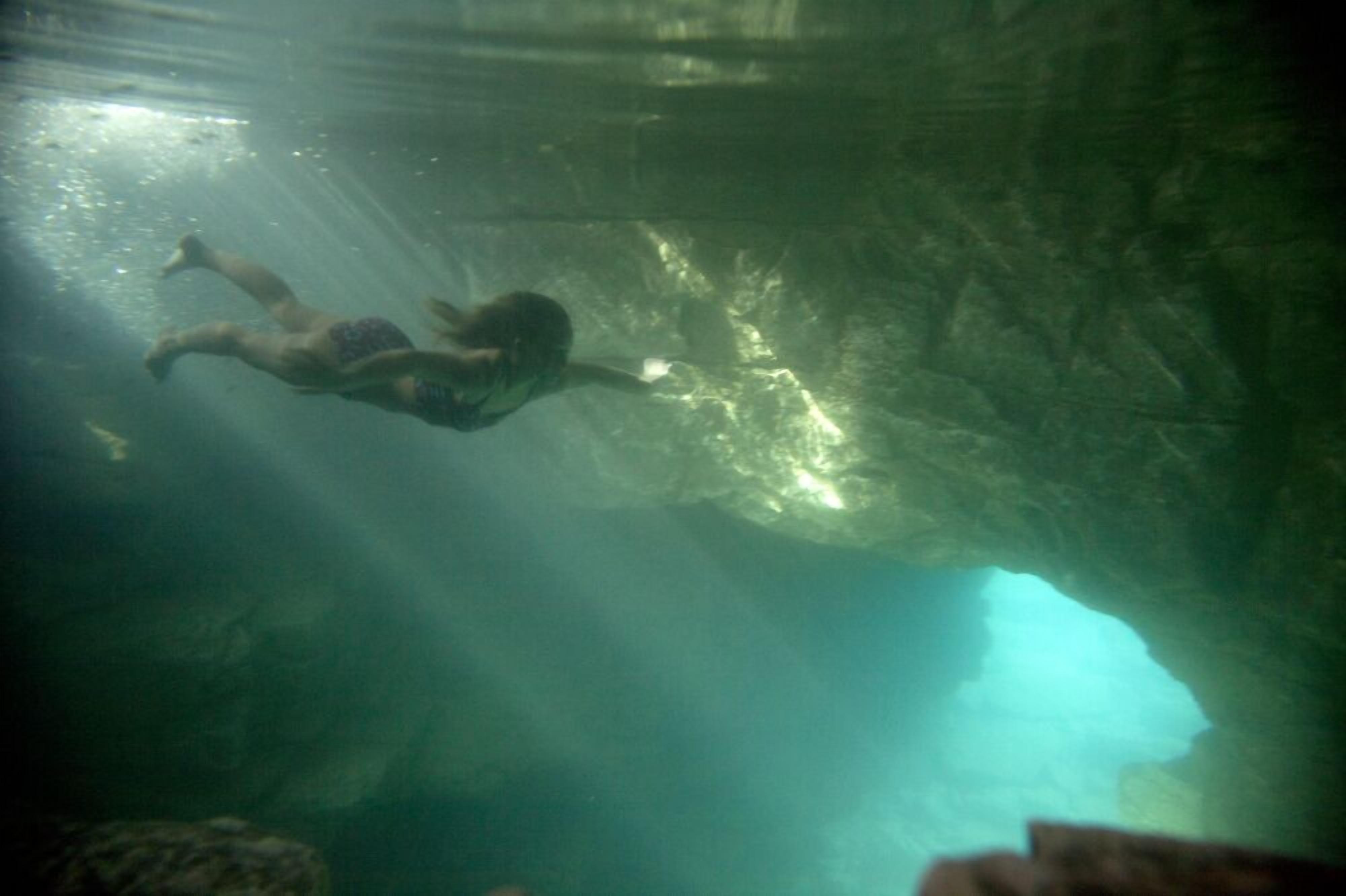 A person swimming underwater in a cave-like environment.