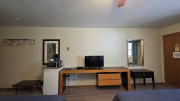 Un dormitorio con cama, escritorio con televisor, microondas y refrigerador pequeño.