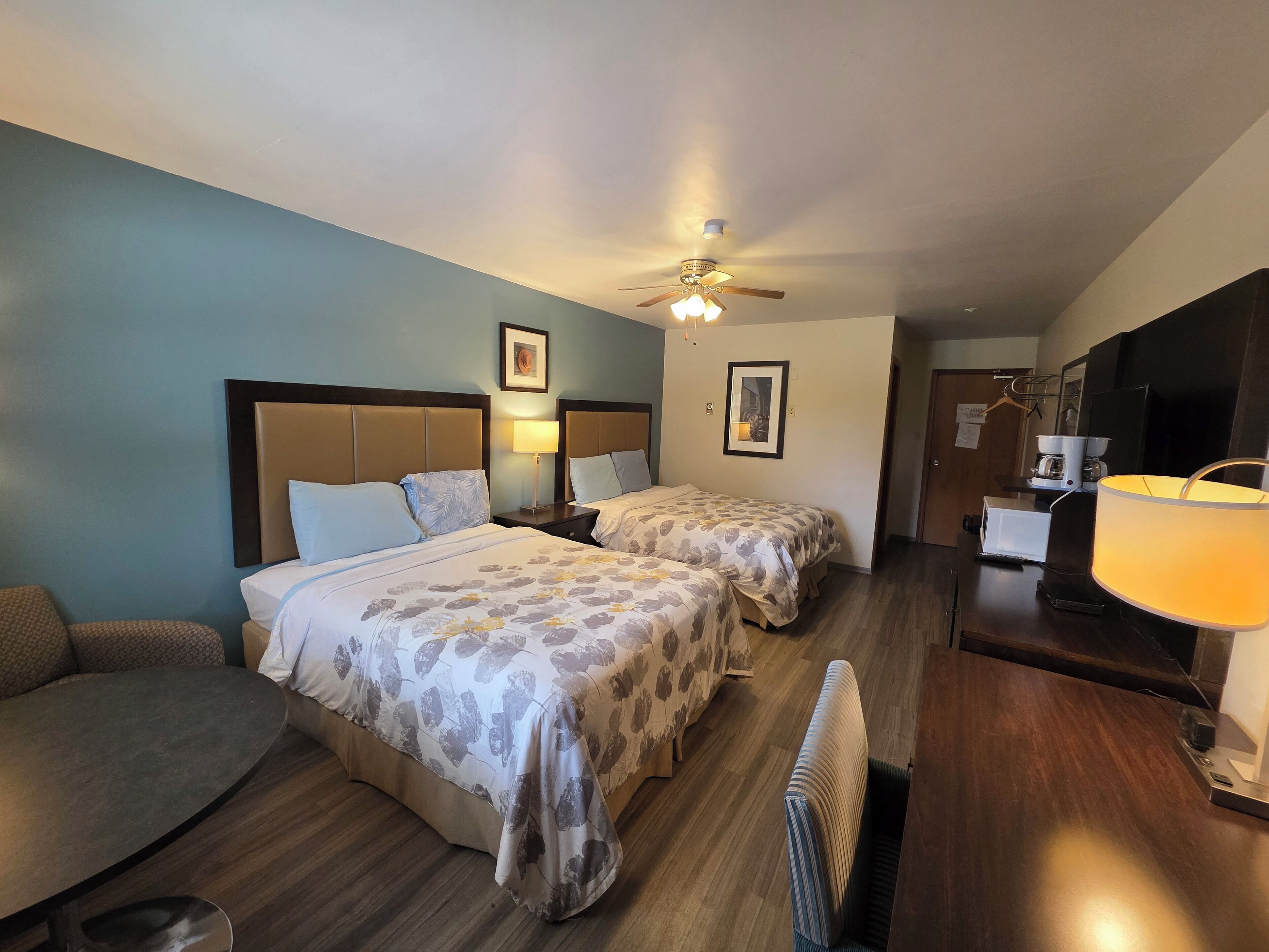 Une chambre d’hôtel avec deux lits, un canapé, un bureau avec une lampe, un ventilateur de plafond et une machine à café.