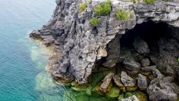 L'entrée d'une grotte côtière rocheuse, avec de l'eau claire et de la végétation luxuriante aux alentours.