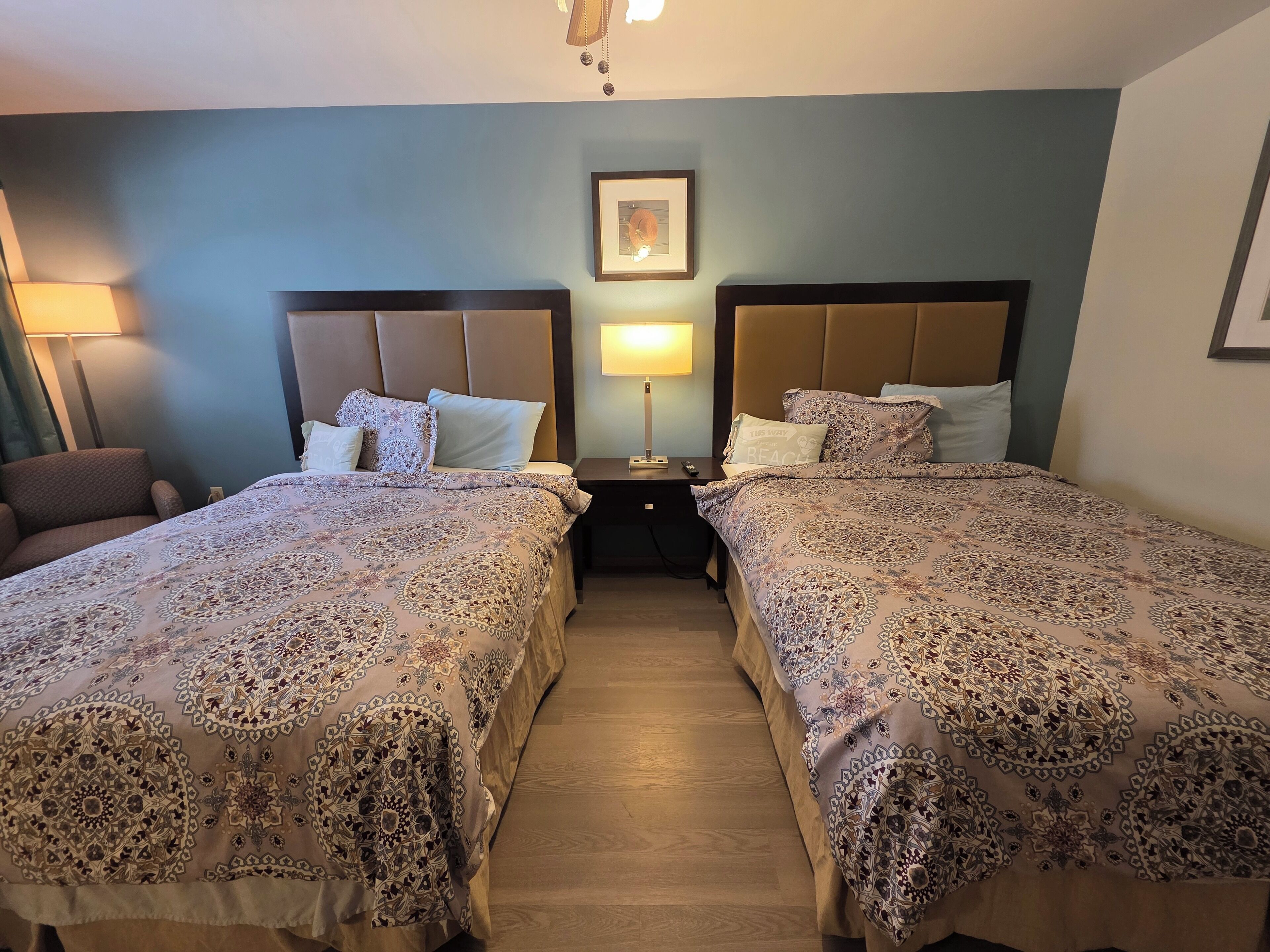 A hotel room with two beds, a nightstand, a lamp, and a framed picture on the wall.