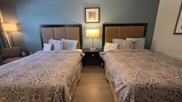 A hotel room with two beds, a nightstand, a lamp, and a framed picture on the wall.