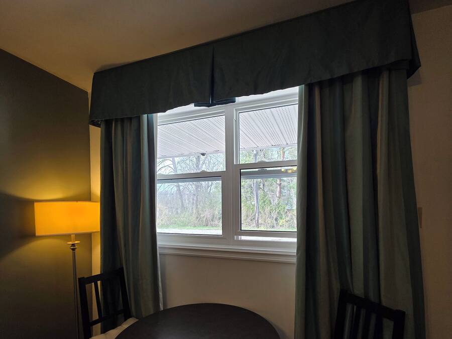 A room with a round table, two chairs, a lamp, and a window with curtains.