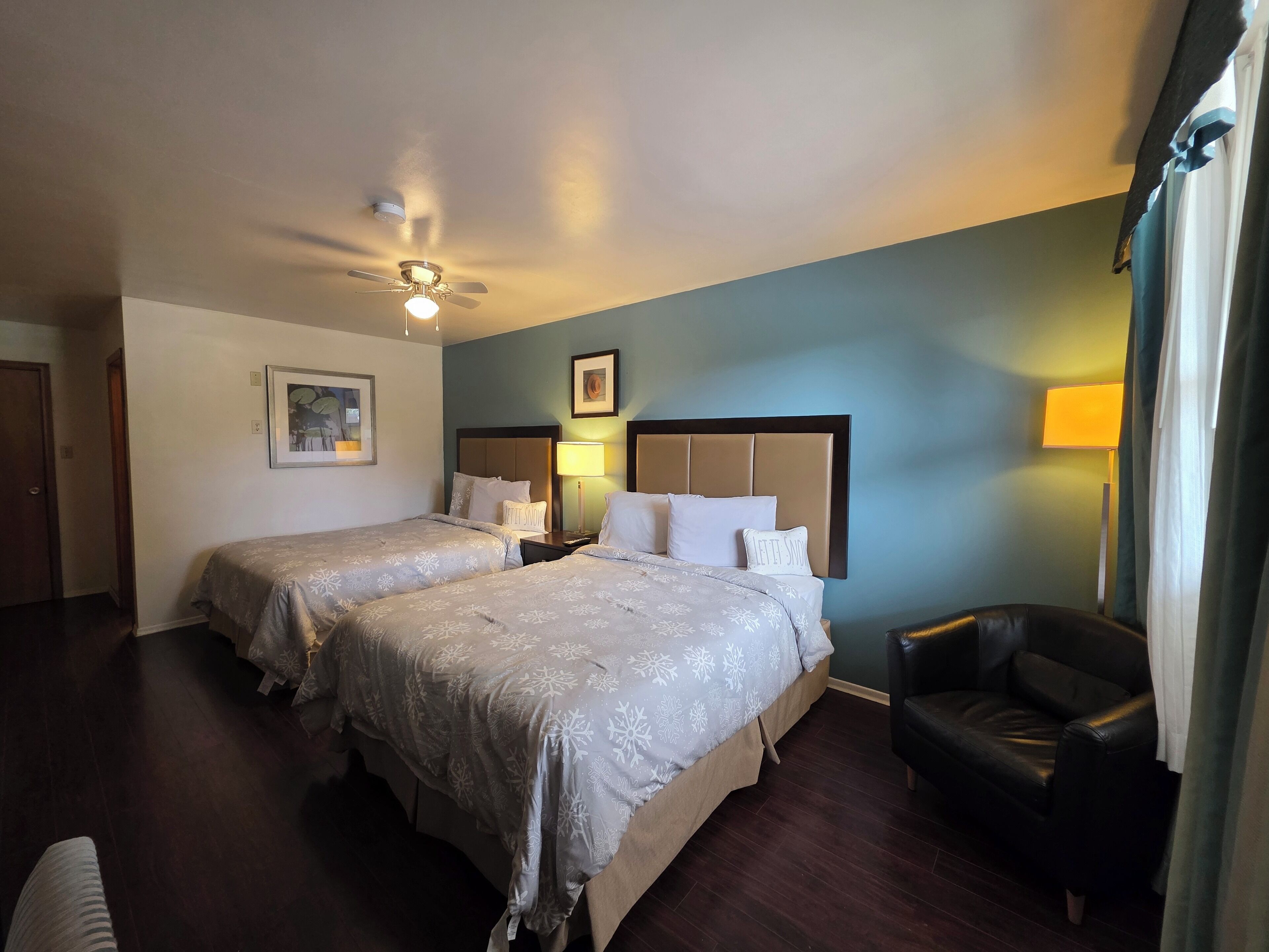 A hotel room with two beds, a ceiling fan, a desk, a chair, and a lamp.