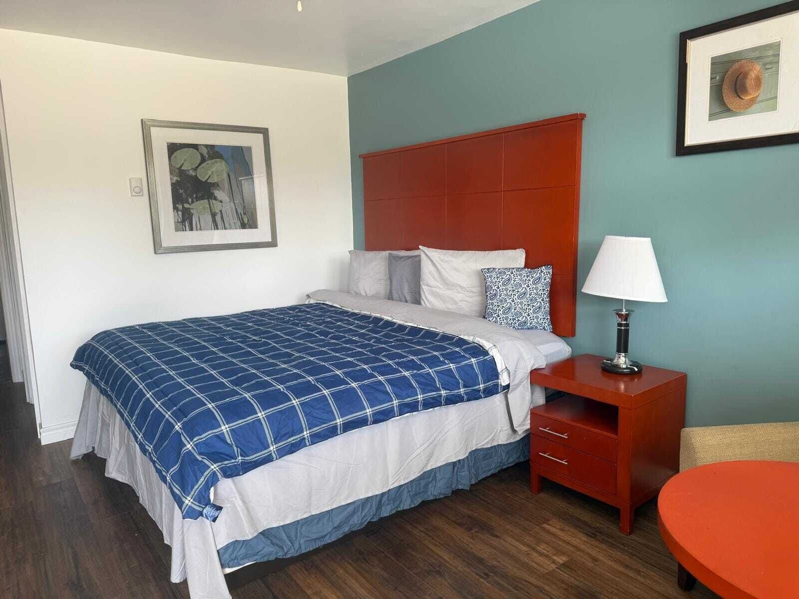 A bedroom with a bed, a nightstand, a lamp, a chair, and a framed picture on the wall.