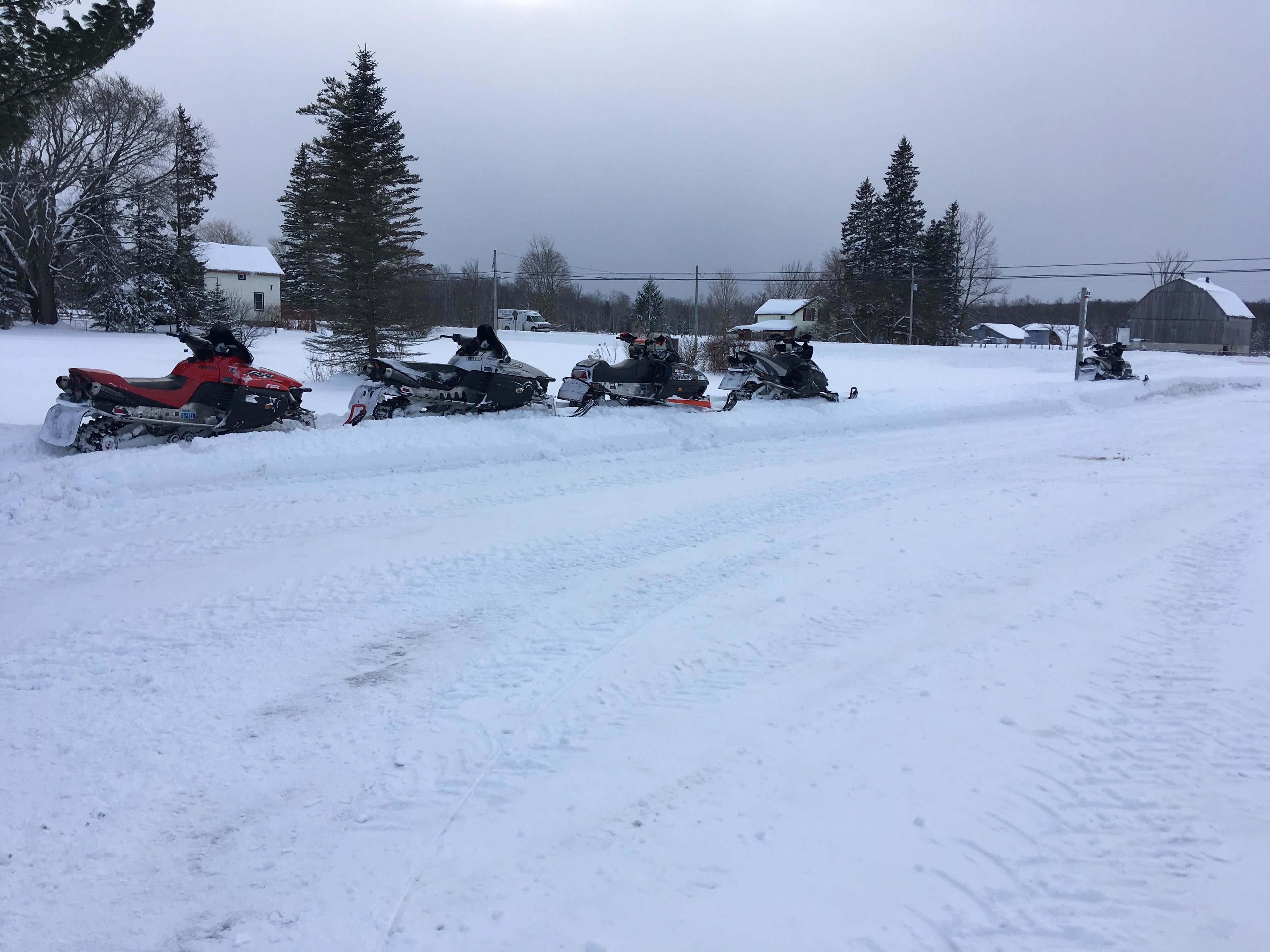 Een besneeuwd landschap met meerdere sneeuwscooters op een rij geparkeerd.