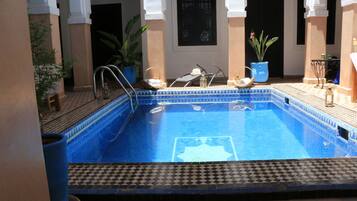Une piscine dont le revêtement est constitué de carreaux disposés selon un motif géométrique, entourée de plantes en pot et dotée d’un sol carrelé.