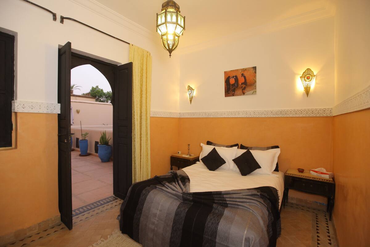 A bedroom with a bed, a nightstand, a wall-mounted lamp, and a painting.