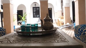 Un interno tradizionale marocchino con un tavolo apparecchiato con teiera e bicchieri, circondato da cuscini decorati e un vassoio ornamentale.