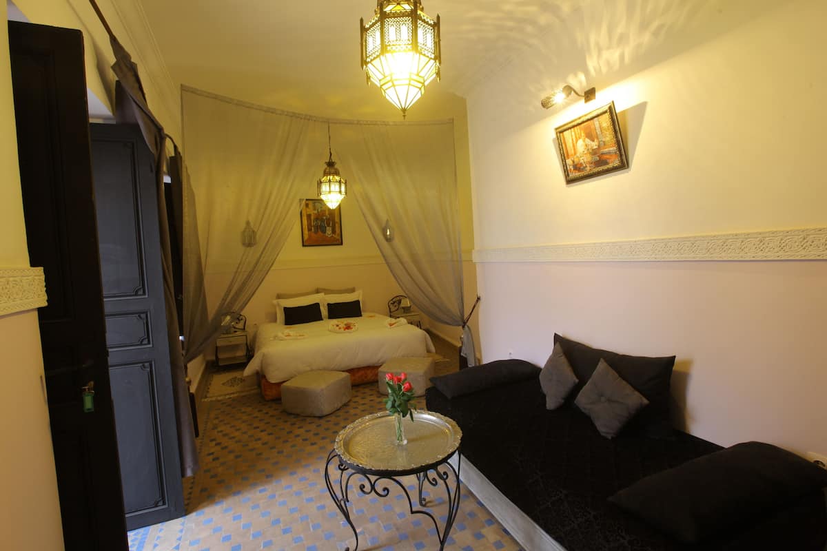 A room with a bed, a sofa, a small table with a vase, and a hanging light fixture.