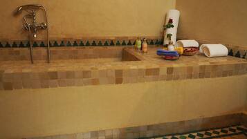 Casa de banho com banheira em mosaico, chuveiro e produtos de higiene pessoal na borda.