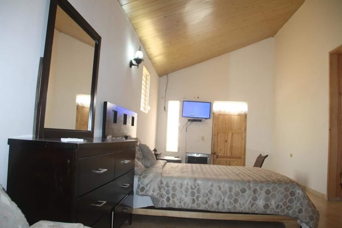 A bedroom with a bed, dresser, TV, and wooden ceiling.