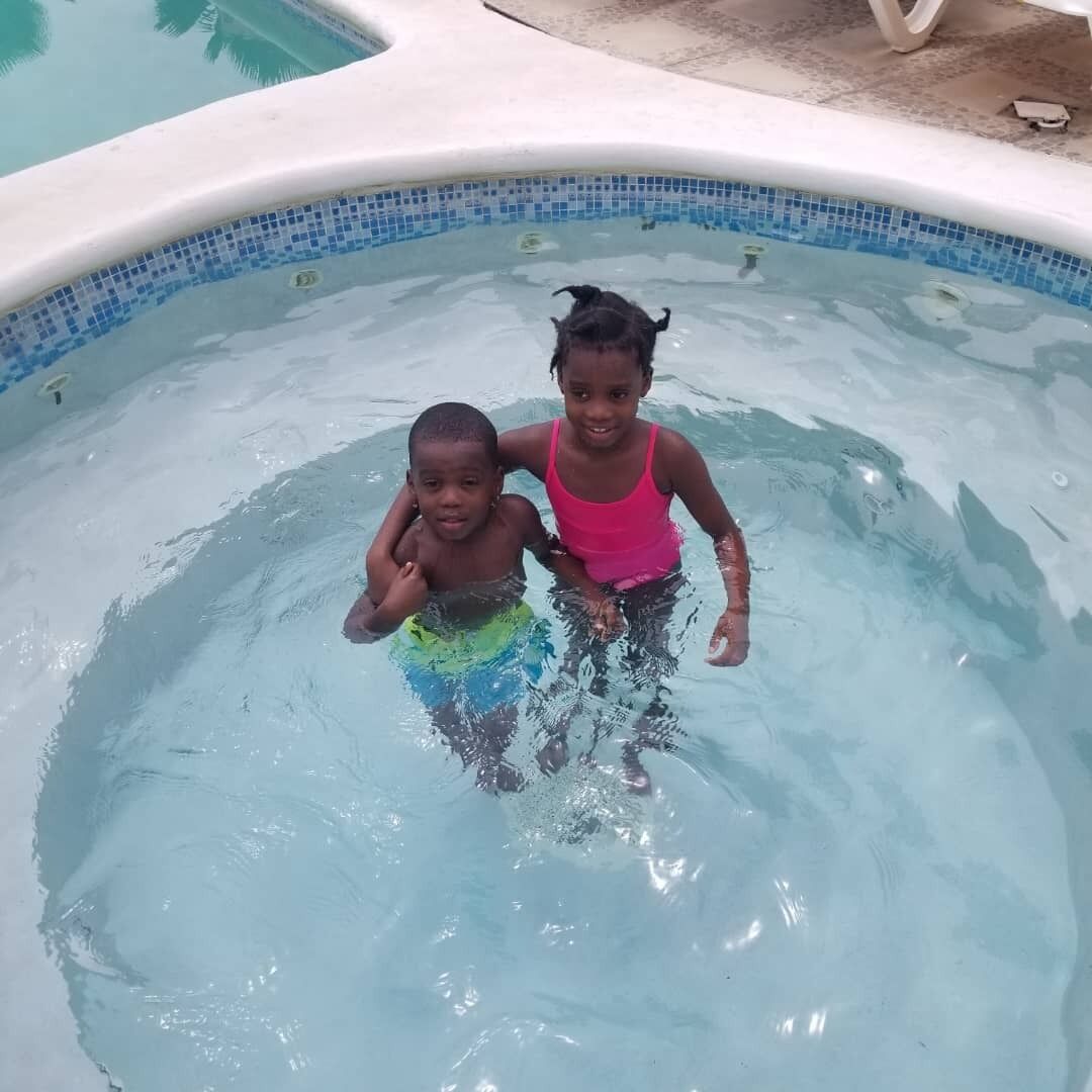 Dos niños en una piscina pequeña y transparente con mosaicos azules.