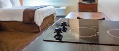 A hotel room with a bed, a TV, and a kitchen area with an induction cooktop.