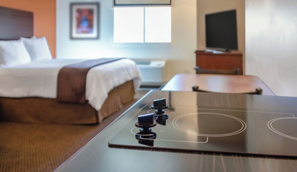 Habitación de hotel con cama, televisión y cocina equipada con placa de inducción.