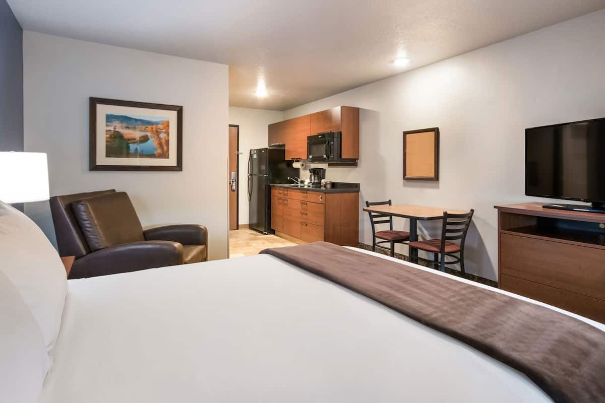 Ein Hotelzimmer mit einem Bett, einem Schreibtisch mit Stuhl, einem Fernseher, einer Küchenzeile und einem gerahmten Bild an der Wand.