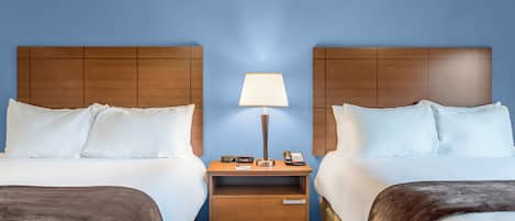 Een hotelkamer met twee bedden, een nachtkastje met een lamp, een telefoon en een klein lade.