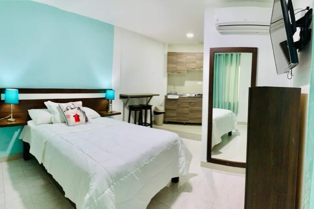 A hotel room with a bed, a desk, a mirror, and a TV.