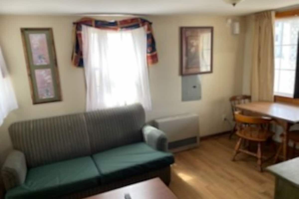 En stue med sofa, spisebord med stole, radiator og billeder i rammer på væggene.