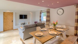 A dining area with a wooden table set for four, a sofa, and a television on the wall.
