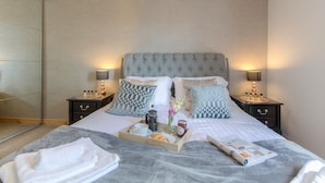 A neatly made bed with a grey blanket, a tray with breakfast items, and a magazine on the bed.