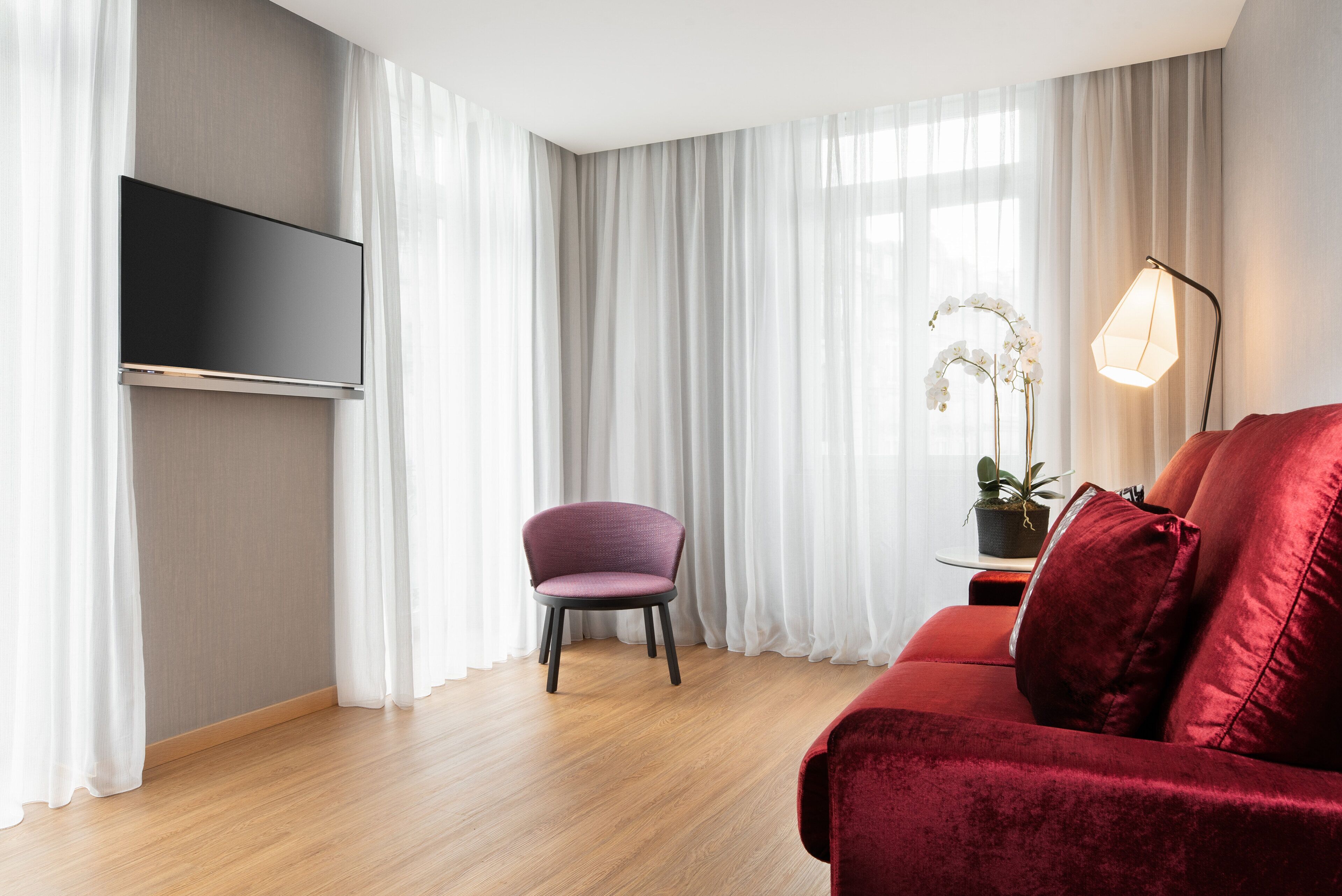 Un soggiorno moderno con una TV a schermo piatto montata a parete, un divano rosso, una poltrona viola e una lampada da terra.