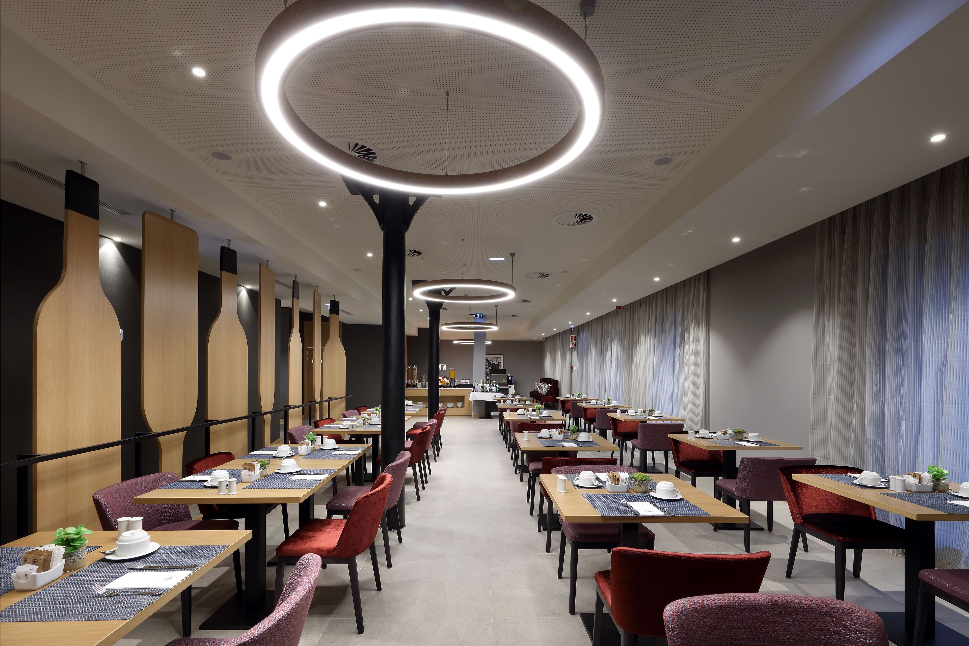Uma sala de jantar moderna com várias mesas e cadeiras, luminárias no teto e uma paleta de cores neutras.