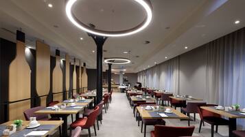 Uma sala de jantar moderna com várias mesas e cadeiras, luminárias no teto e uma paleta de cores neutras.
