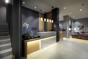 Un área de recepción moderna con mostrador de mármol, detalles de madera y una escalera.