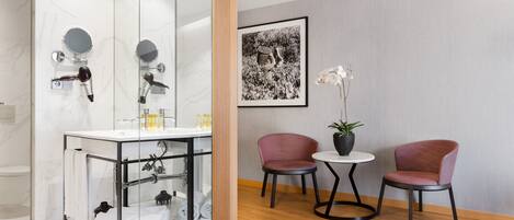 A modern bathroom with a glass shower enclosure, a vanity with a mirror, and two chairs by a small table.