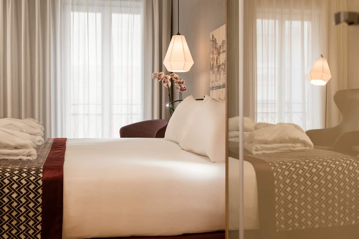 A hotel room with a large bed, a bedside table with a lamp, and a mirror.