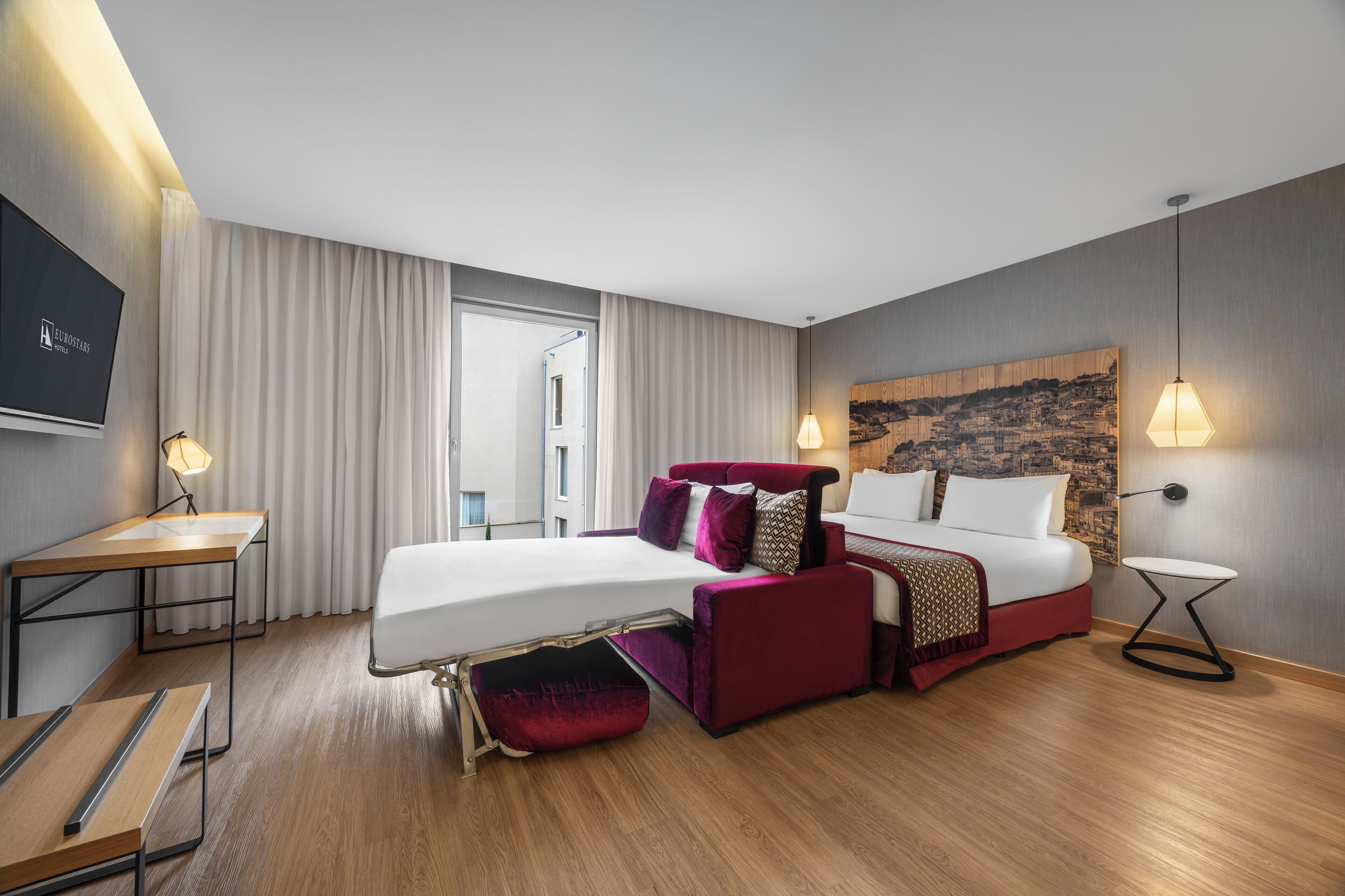 A modern hotel room with a bed, a desk, and a TV.
