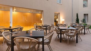 An outdoor dining area with wicker chairs and tables, a glass partition, and a warm interior light. - Eurostars Porto Centro (Porto)