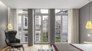 A modern hotel room with a large window, a bed, a chair, and a small table. - Eurostars Porto Centro (Porto)