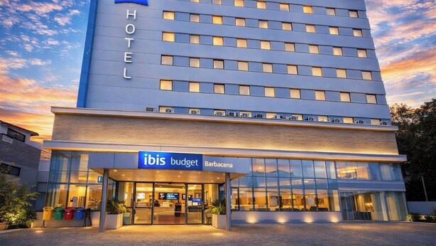 Ein modernes Hotel mit einem gut sichtbaren 'ibis budget'-Schild, einer Glasfassade und einem 'Barbacena'-Schild.