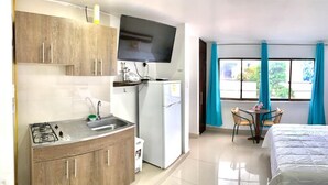 A hotel room with a kitchenette, a bed, a TV, and a window with curtains. - Bahia Tropical III (San Andrés)