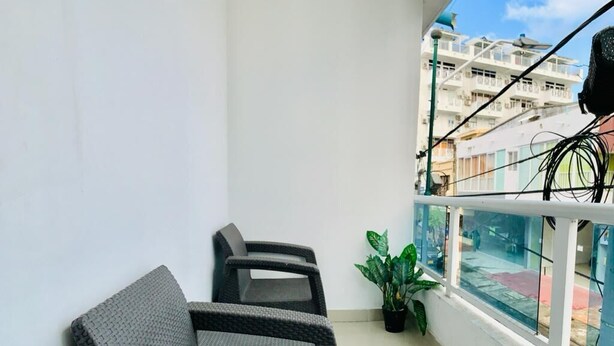 A balcony with two grey wicker sofas, a potted plant, and a view of a building with balconies. - Bahia Tropical III (San Andrés)