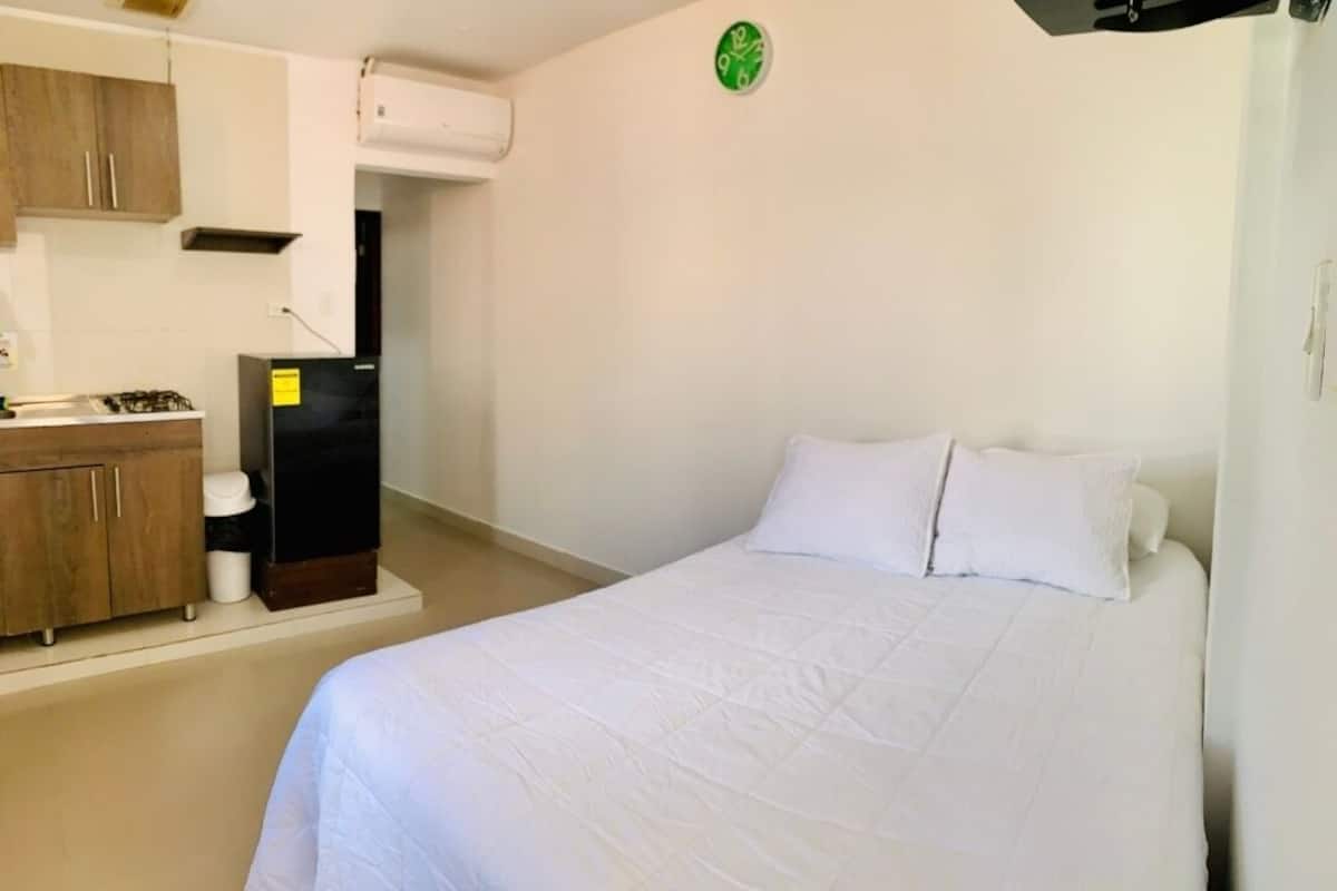 Ein Schlafzimmer mit einem Bett, einer kleinen Küchenzeile mit Herd und Kühlschrank sowie einer Uhr an der Wand.