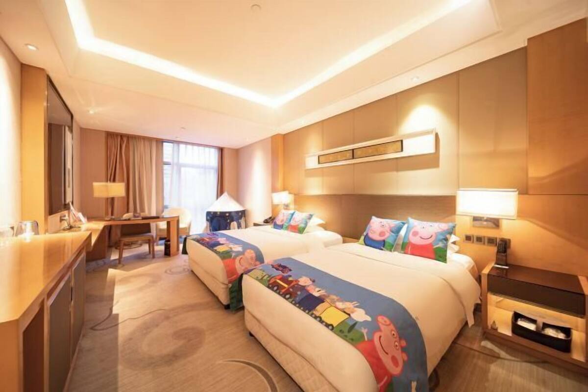 A hotel room with two beds, a desk, a chair, a lamp, and a large window.