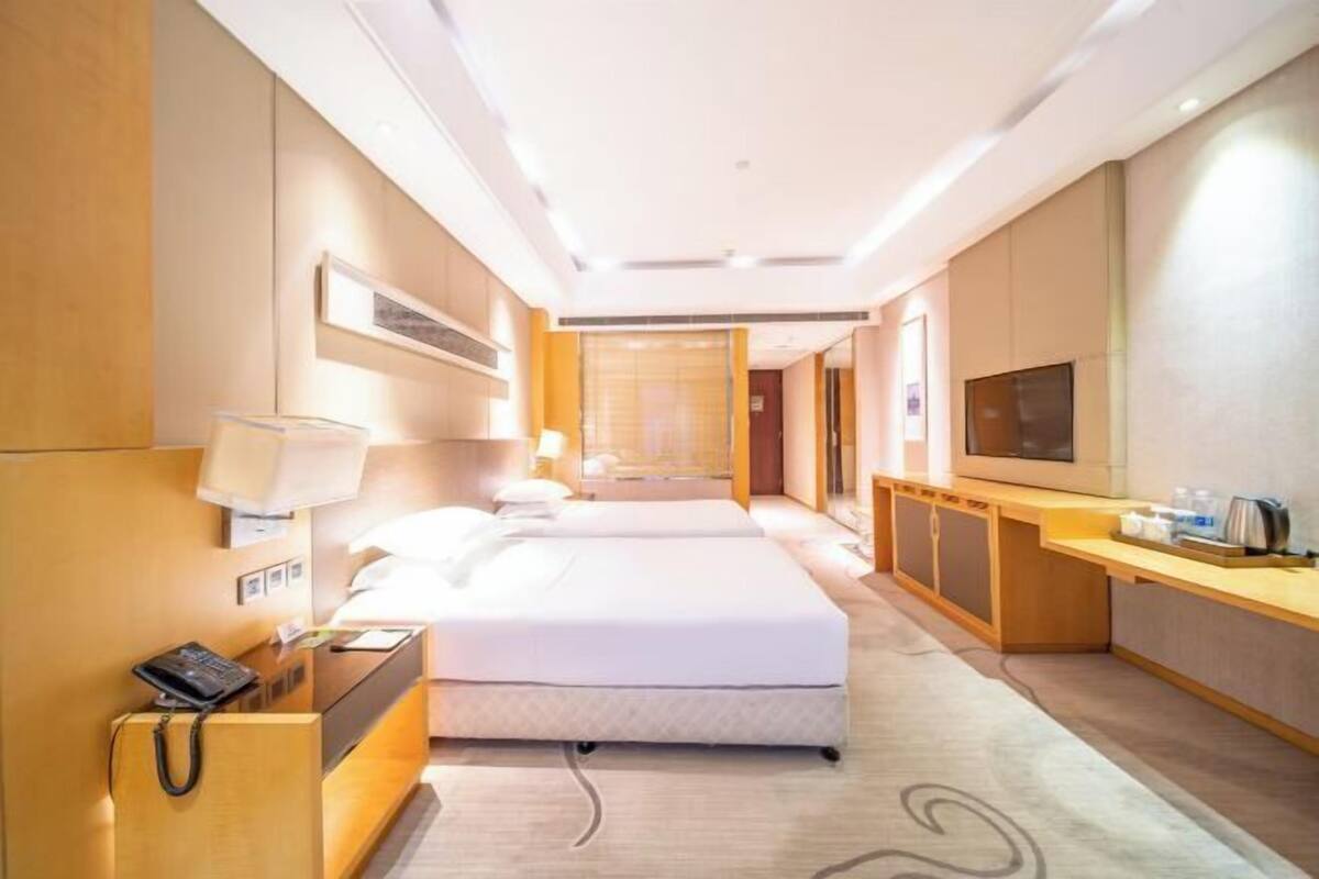 A hotel room with a bed, bedside table, lamp, and a TV on the wall.