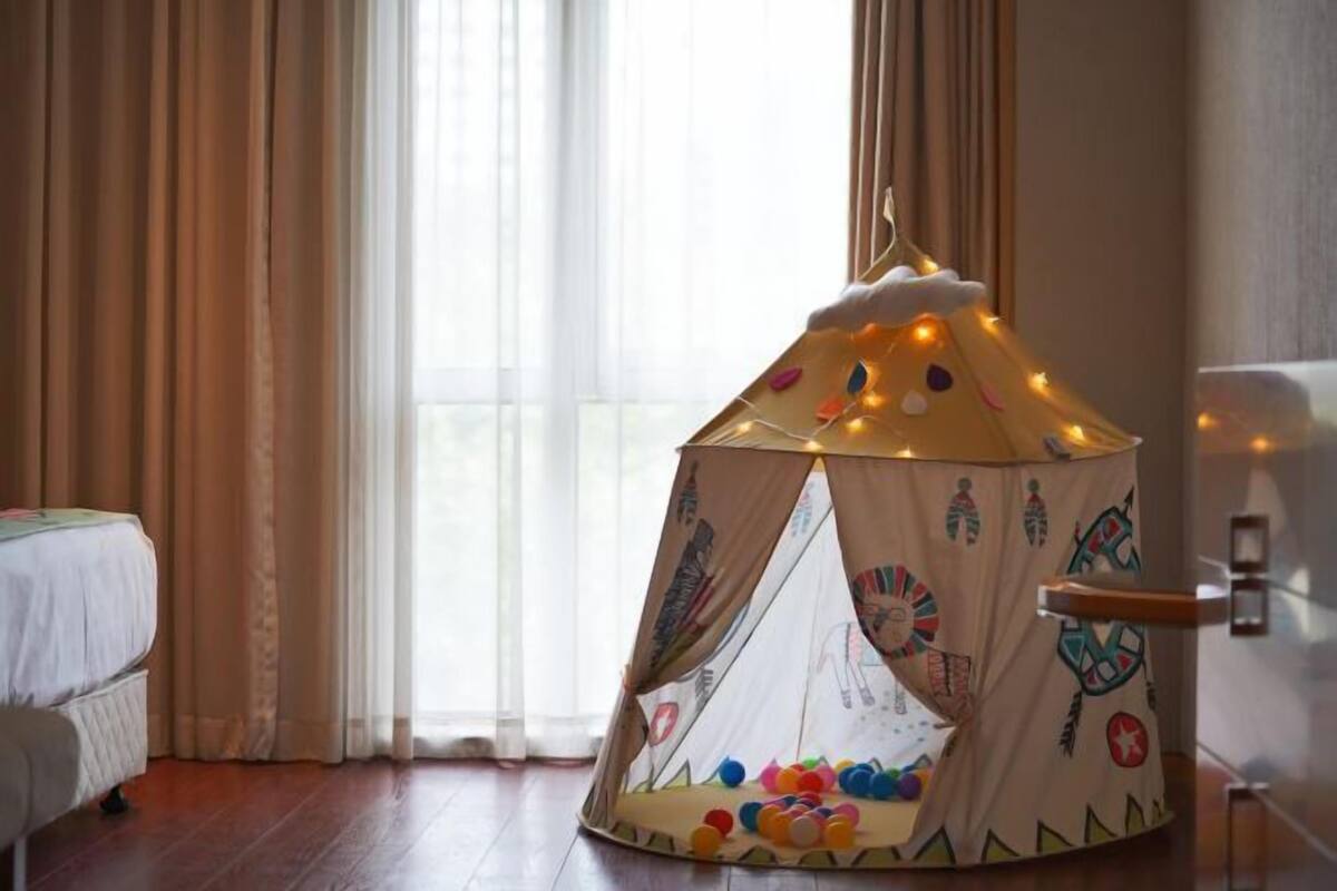 A tent with colorful decorations and lights, a bed, and a window with curtains.