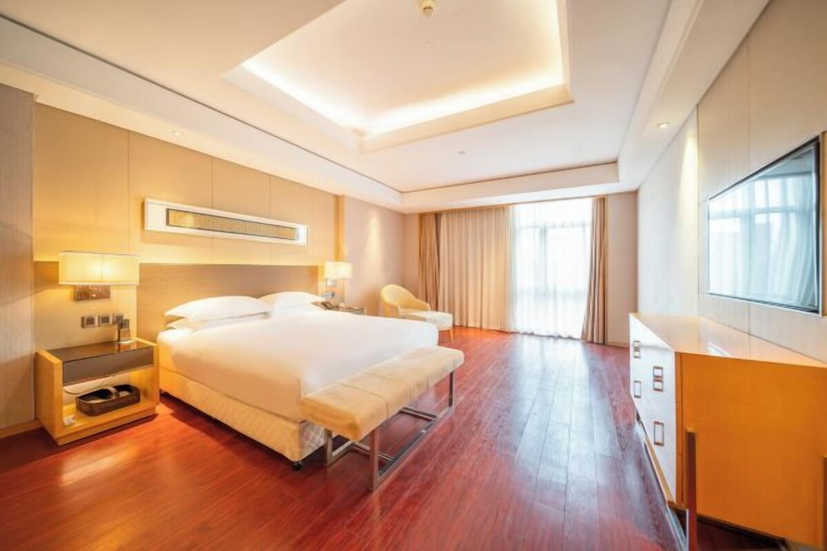 A modern hotel room with a large bed, bedside tables, a desk, and a TV.
